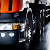Closeup Of The Front Of A Truck Trailer With A Mechanic Inspecting The Rear End Of The Trailer In The Background During A DOT Trailer Inspection