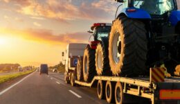 A Step Deck Trailer Hauling Two Farm Vehicles on a Highway With the Sun Setting in the Background Business Growth With Pinnacle Trailers