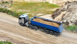 A Blue Dump Trailer Being Pulled by a Silver Truck Driving on a Dirt Path Loaded With Sand Dump Trailers For Sale